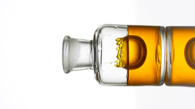 Drop of argan oil is falling down into old fashioned bottle
