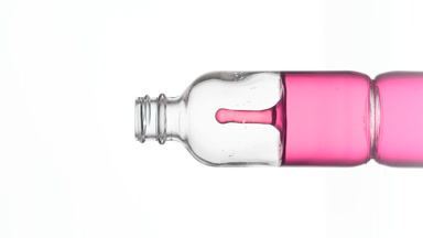 Drop of retinol falls down into medical bottle with pink fluid