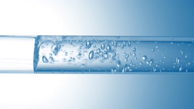 Transparent liquid flows in glass tube creating bubbles