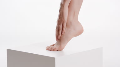 Slim female model touches her smooth leg on white cube platform