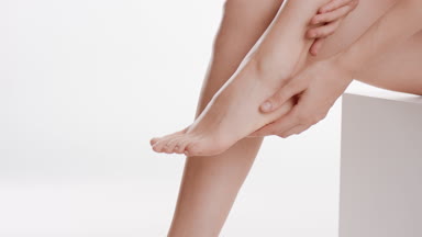 Slim woman touches her foot and calf sitting on white platform
