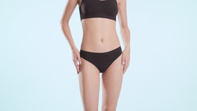 Young woman strokes hips and waistline and turns from the camera
