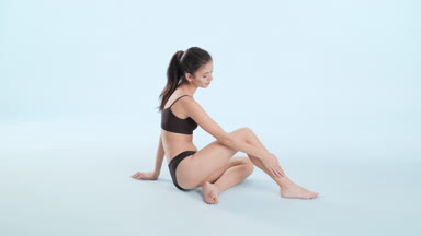 Asian woman in bikini with long dark hair strokes leg sitting