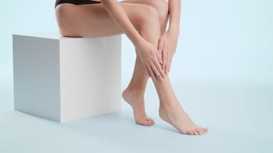 Gorgeous woman strokes smooth leg sitting on white cube platform