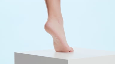 Woman strokes her tiptoe foot on the white cube platform
