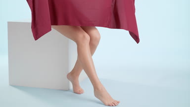Woman throws a piece of red cloth down her legs sitting on cube