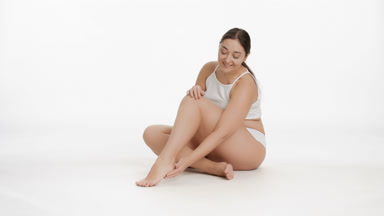 Young Caucasian plus size woman strokes foot and leg smiling