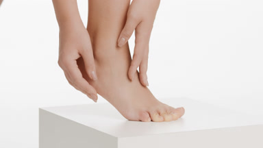Female model strokes her foot and leg on white cube platform