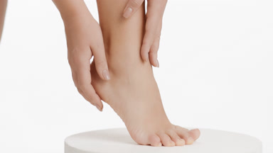 Female model strokes heel and leg on white round platform