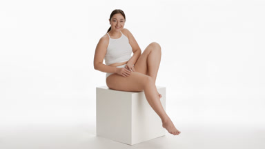 Plus size woman strokes thigh sitting on white cube platform