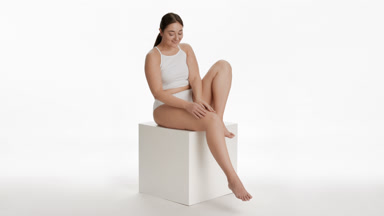 Young plus size woman strokes leg sitting on white cube platform