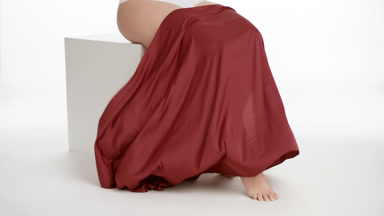 Woman throw a piece of red cloth down her legs sitting on cube