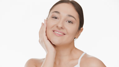 Plus size brown-haired woman in white top touches face smiling