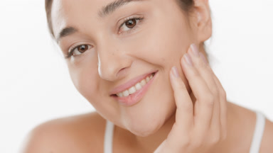 Young Caucasian dark-haired woman strokes her cheek smiling