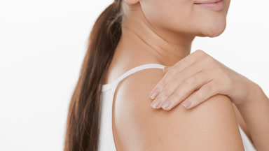 Woman strokes shoulder, turns to camera smiling and touches chin