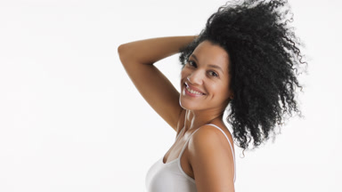 African American slim woman in white top touches curly dark hair
