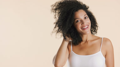 African woman turns to camera touching curly hair and smiling