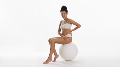 African woman strokes leg and puts hand on waist sitting on ball