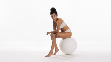 Young woman strokes leg and puts hands on knees sitting on ball