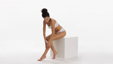 African fit woman strokes leg sitting on cube podium and smiling