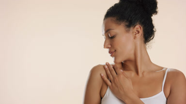 Gorgeous African woman strokes clavicle and shoulder smiling