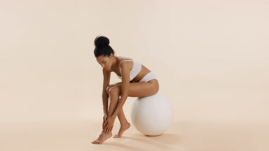African woman strokes leg sitting on big white ball and smiling