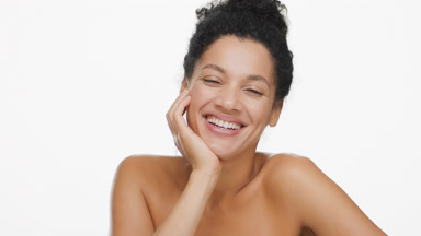 African woman with dark curly hair in bun touches face laughing