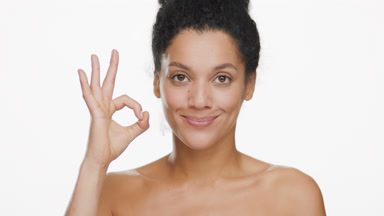 Pretty African American woman blinks and shows OK sign smiling