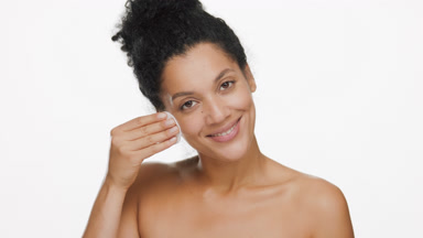 African American woman strokes cheek with cotton pad smiling