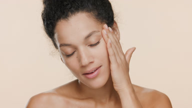 Slim African woman with black curly hair strokes face and smiles