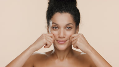 African woman with bare shoulders stretches cheeks and smiles