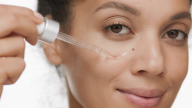 Pretty African woman drips serum on cheek from dropper smiling