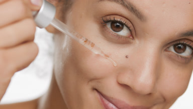 Cute African woman drips serum on her cheek from dropper smiling