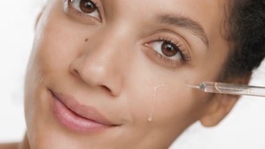 Young African woman drips serum on cheek from pipette smiling