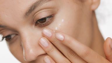 Beautiful African woman applies face care cream on cheek smiling