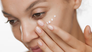 Woman applies cream on cheek and looks at the camera smiling