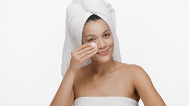 African woman with a towel on hair strokes cheek with cotton pad