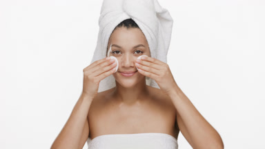 Young woman with towel on head strokes cheeks with cotton pads