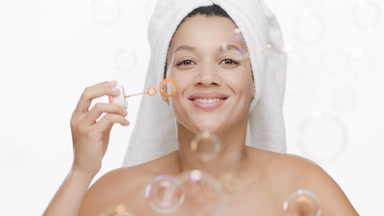 Cute African woman with towel on hair blows soap bubbles smiling