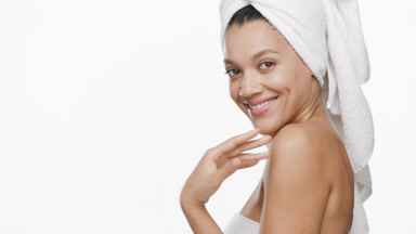 Woman with towel on hair stokes collar bones turning and smiling
