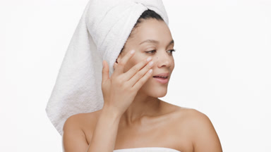 African woman with a towel on hair strokes cheek and turns head