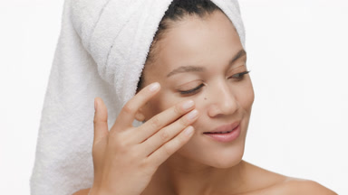African woman with a towel on head strokes cheek turning head