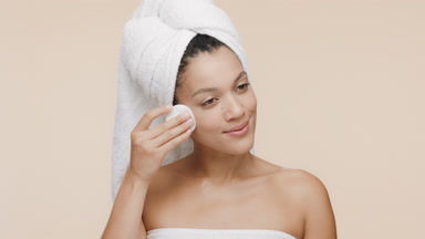 African woman strokes her nose and cheek with cotton pad smiling