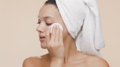 African woman strokes nose, cheeks and jaw line with cotton pad