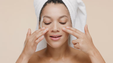 African woman with towel on head stokes nose and cheeks smiling