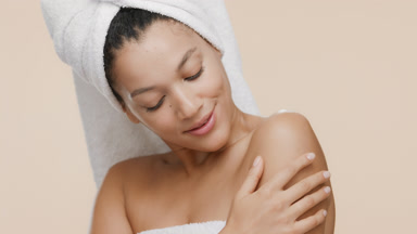 African slim woman with a towel on hair stokes shoulder smiling