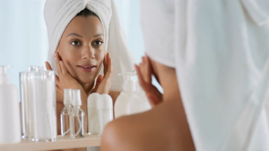 African woman touches face and shoulders in front of the mirror
