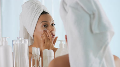 Woman strokes face and decides to apply cream in front of mirror