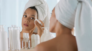 Woman strokes face with cotton pad and smiles in front of mirror