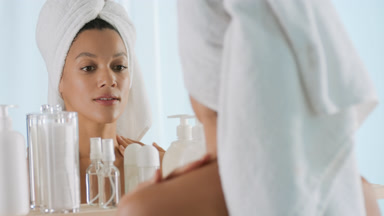 African woman with towel on head strokes body in front of mirror